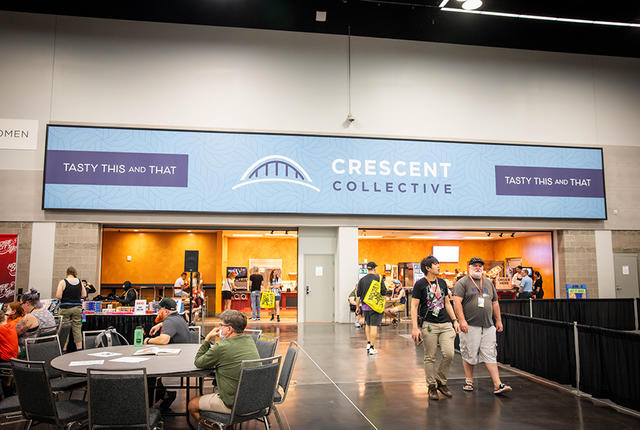 A big blue sign that says "Crescent Collective" hangs over a small commissary inside an exhibit hall.