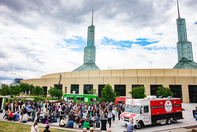 Three food trucks in an outdoor plaza filled with guests